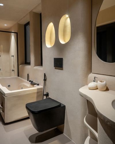 Beige plaster bathroom with black wall-hung toilet, freestanding tub, and two eye-shaped wall sconces