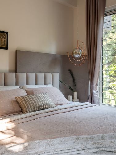 Bed with pink bedding and channel-tufted headboard beneath a sculptural pendant light near a window