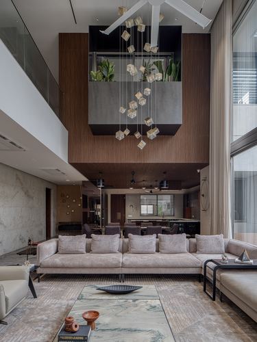 Double-height living room with cascading cube chandelier, beige sectional sofa, and wood-clad mezzanine box above