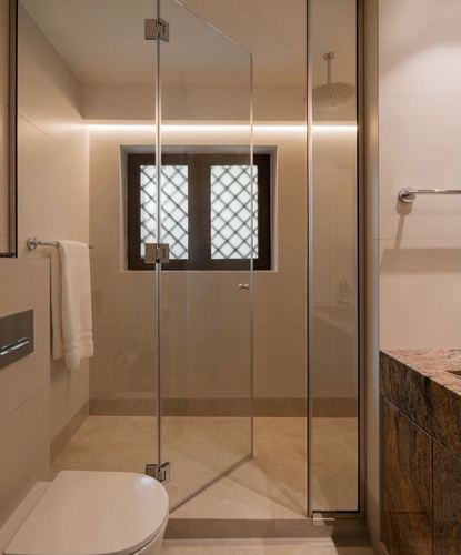 Minimal beige bathroom with frameless glass shower, lattice window, and stone-clad vanity counter