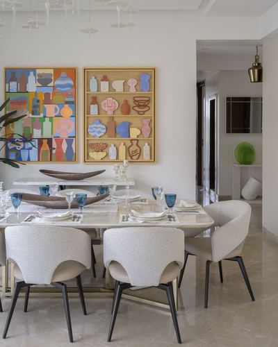 Dining table set with blue glassware beneath two framed decorative art panels and boucle chairs