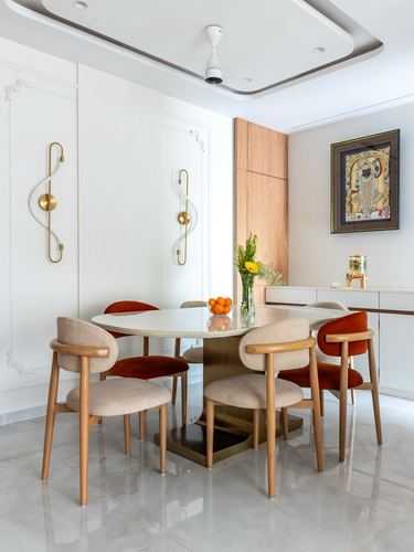 Round marble dining table with mixed wicker and velvet chairs beneath brass sconces