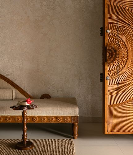Carved wooden daybed and side table beside a heavily carved wooden door against a textured plaster wall