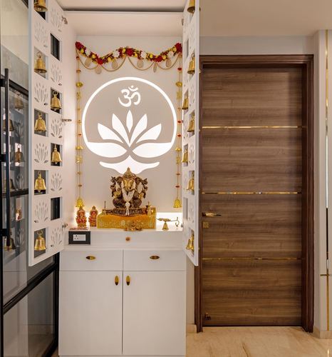 White pooja unit with backlit om lotus motif, ganesha idol, jali doors and hanging bells beside wooden door