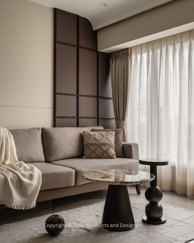 Beige living room with walnut paneled wall, gray sofa, and stone-topped pedestal tables by window