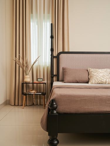 Bedroom corner with black four-poster bed, mauve linens, and bedside table by curtained window