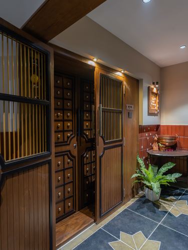 Wooden entry door with brass-knobbed drawer motifs beside a fern in a Pune home foyer