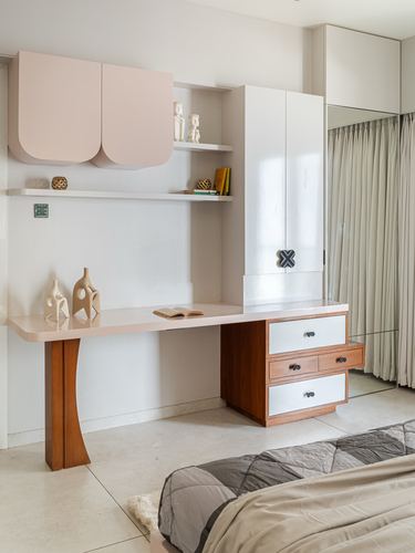 Bedroom study nook with blush cabinetry, wooden desk on curved leg, and mirrored wardrobe beside bed