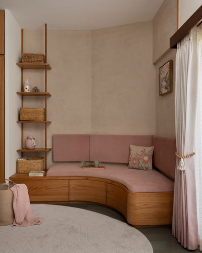 Curved wooden bench with pink cushions in a plastered corner nook with ladder shelving