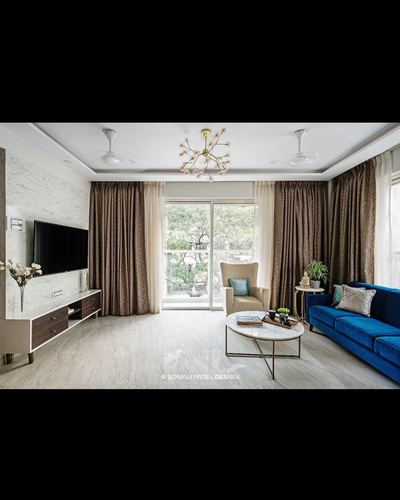 Living room with blue velvet sofa, marble tv wall, and balcony view through sheer curtains