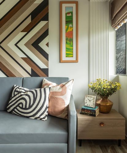 Living room corner with blue sofa, patterned cushions, wood chevron wall art, and wooden side table with flowers