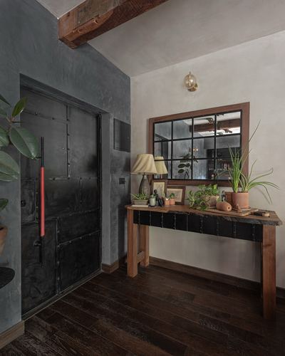 Entryway with black riveted metal door, wooden console table, mirror, and potted plants on dark wood floor