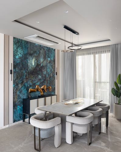 Dining room with curved grey chairs around stone table beneath teal feature wall and ring pendant lights