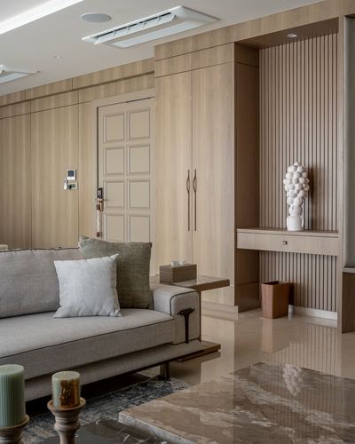 Wood-panelled foyer with fluted niche console and sculptural vase beside living room sofa