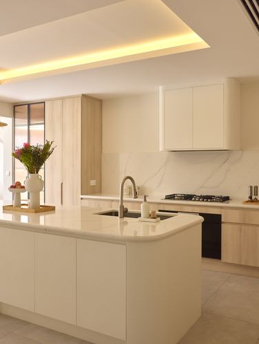 Bright minimalist kitchen with island, light wood cabinetry, and marble-look backsplash under a cove-lit ceiling