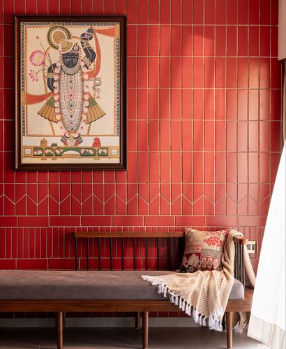 Red tiled wall with framed pichwai painting above a wooden bench with cushions