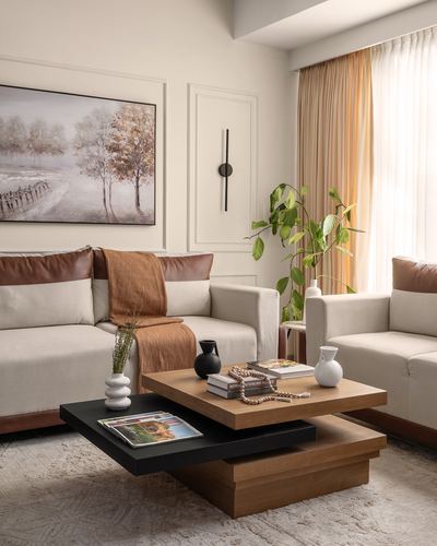 Beige living room with two sofas, layered wood coffee table, and framed landscape painting