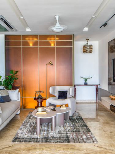 Living room with copper wall panel, curved chair, round nesting tables on patterned rug