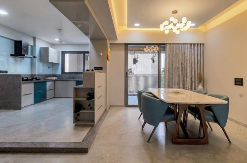 Open dining and kitchen area with marble floors, teal chairs and a spherical chandelier