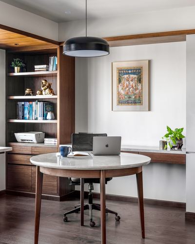 Home office with round marble table, fluted wood shelving, and framed miniature painting on wall