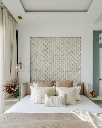Bed with cream cushions beneath a woven textured headboard niche and a glass globe pendant light