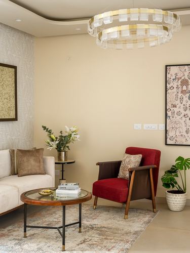 Living room corner with cream sofa, red armchair, round glass coffee table, and layered chandelier.