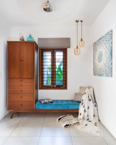 Foyer with teak wardrobe, teal velvet window seat, and amber pendant lights beside a barred window