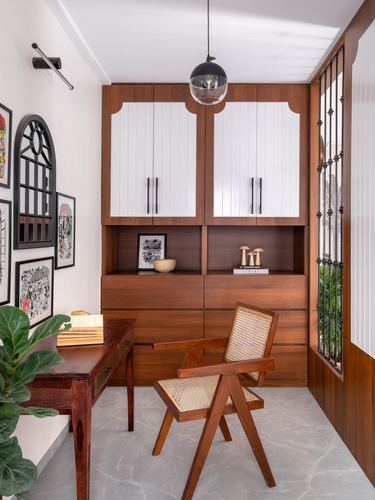 Wooden study nook with cane armchair, desk, two-tone cabinets and pendant light