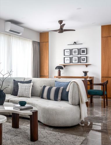 Living room with curved grey sofa, wood paneling, gallery wall, and marble flooring