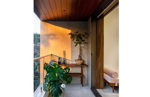 Balcony corner with wooden ceiling, stone wall, console table, and large monstera plant in golden light