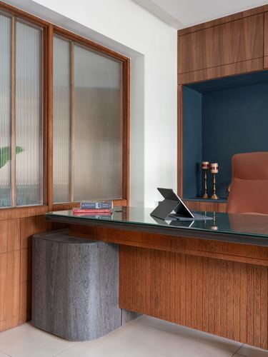 Wooden desk with glass top beside reeded glass window and navy velvet niche