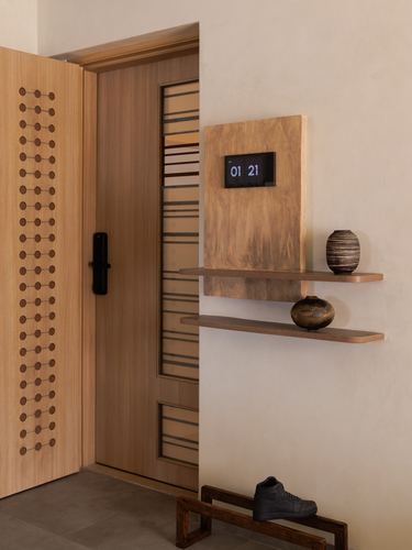 Entryway with carved wooden door, floating shelves holding ceramic vases, and a digital clock