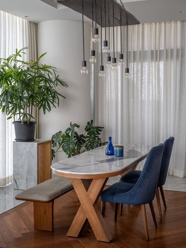 Dining nook with marble-top table, cross-leg wood base, blue velvet chairs, bulb chandelier, sheer curtains