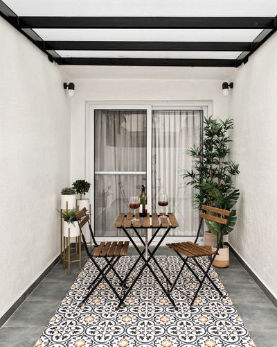 Narrow covered balcony with bistro table, folding chairs, plants and patterned tile rug