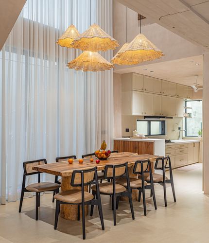 Dining table with cane chairs under woven pendant lights, kitchen visible beyond