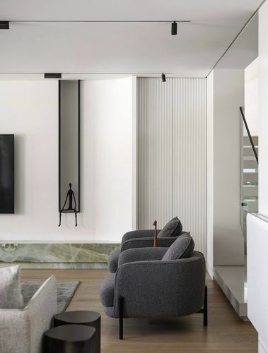 Two curved boucle armchairs in a minimalist living room with a niche sculpture and marble base