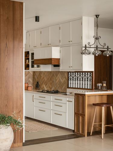 Warm-toned kitchen with white cabinetry, herringbone wood backsplash, and iron window grille