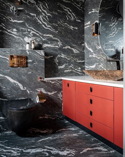 Dark veined marble bathroom with red lacquered vanity, black toilet, and stone vessel sink