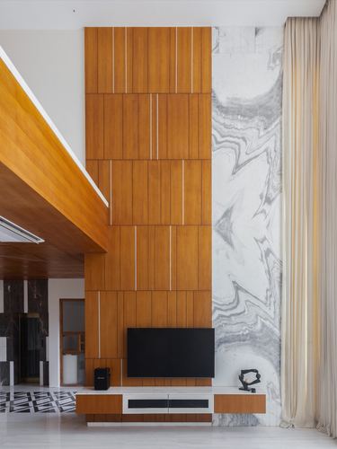Double height living wall with grooved wood panelling beside veined marble and mounted television