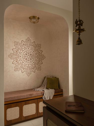 Arched pink plaster niche with mandala stencil above a wooden bench with cane-inset cabinets