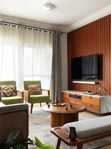 Living room with ribbed wood tv wall, green cane armchairs, and round wooden coffee table.