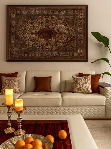 Cream quilted leather sofa beneath a large framed carpet artwork, with candles and citrus on a wooden table.