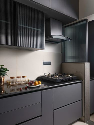Grey modular kitchen corner with fluted glass cabinets, chimney hood, and dark stone countertop