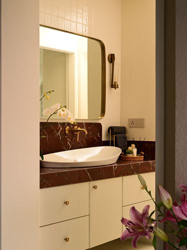 Bathroom vanity with red marble counter, oval sink, arched brass mirror and fluted cabinetry