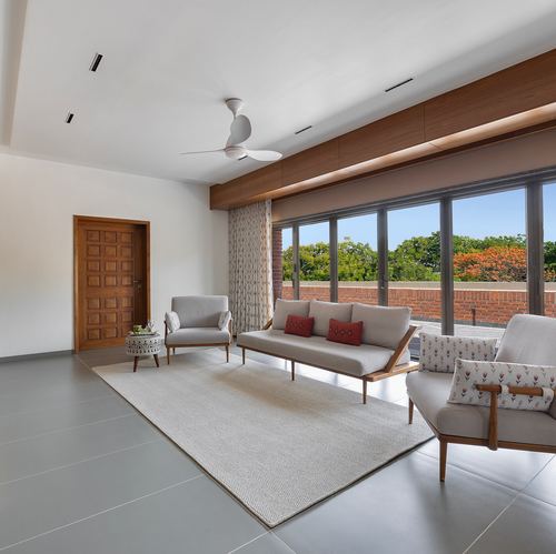 Grey-toned living room with wooden panelled door, ceiling fan, and full glass wall opening to brick balcony and trees
