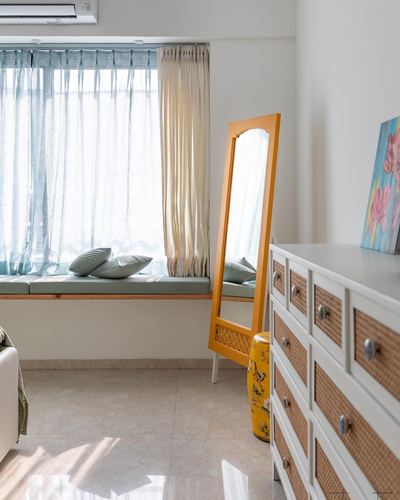 Bright bedroom corner with window seat, mustard-framed mirror, and cane-front dresser