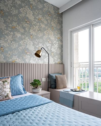 Bedroom with floral wallpaper, fluted taupe headboard, blue quilted bedding and gold arc lamp beside a balcony window