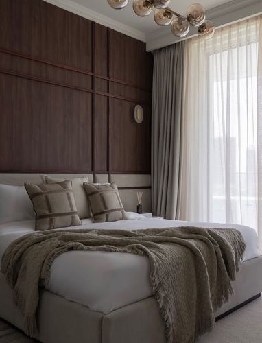Bedroom with dark wood paneled headboard wall, sheer curtains, and neutral upholstered bed with fringed throw