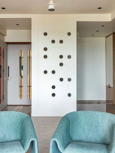 Foyer with teal velvet armchairs facing a white wall of circular perforations