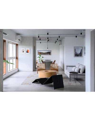 Open-plan minimal living and dining space with round wood table, cane chairs, and exposed track lighting